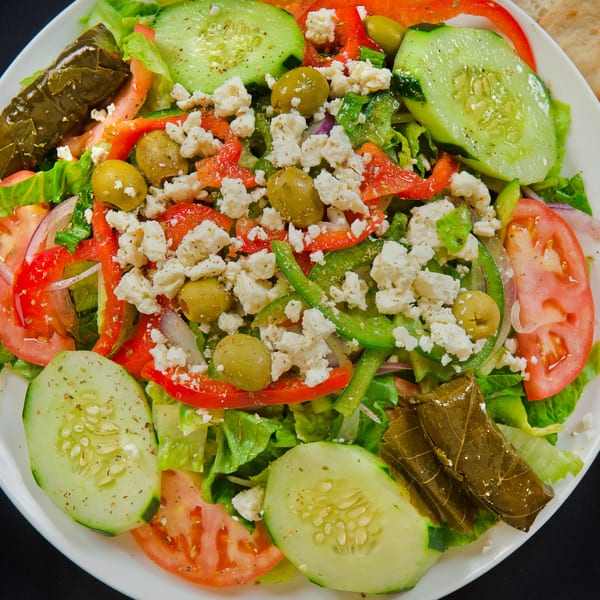 A vibrant Afghan salad with lettuce, tomatoes, cucumbers, bell peppers, olives, feta, and stuffed grape leaves.