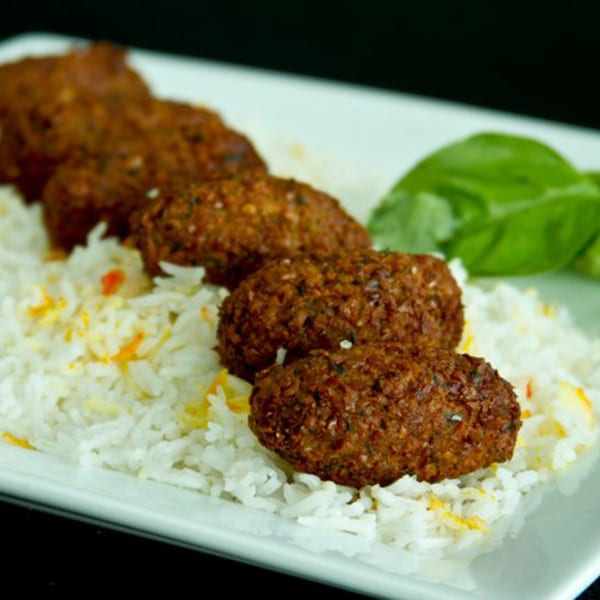 Four brown falafel-like patties on a bed of white rice with green garnish on a white plate.
