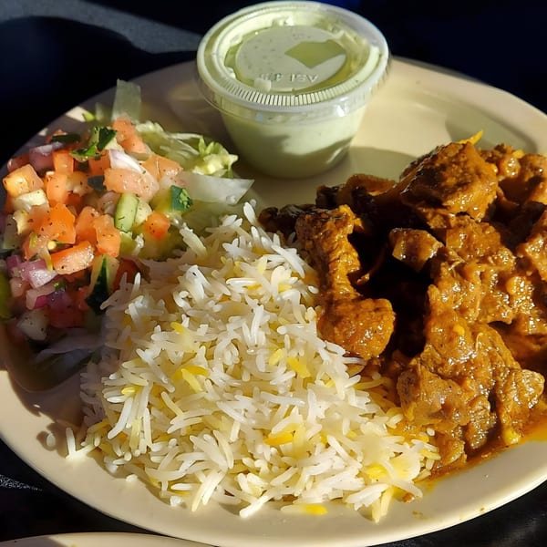 Mimi's Kabob's Afghan dish with rice, meat stew, a side salad, and a cup of green sauce.