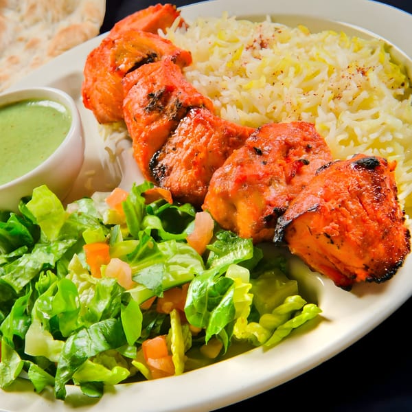 Mimi's Kabob chicken tikka, rice, green salad, and chutney on a white plate.