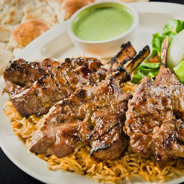Mimi's Kabob's grilled lamb chops with rice, green sauce, and salad on a white plate.