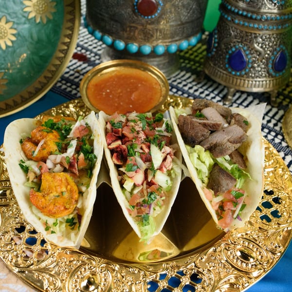 Three Afghan tacos, one with shrimp, one with chicken, and one with beef, on a gold platter.