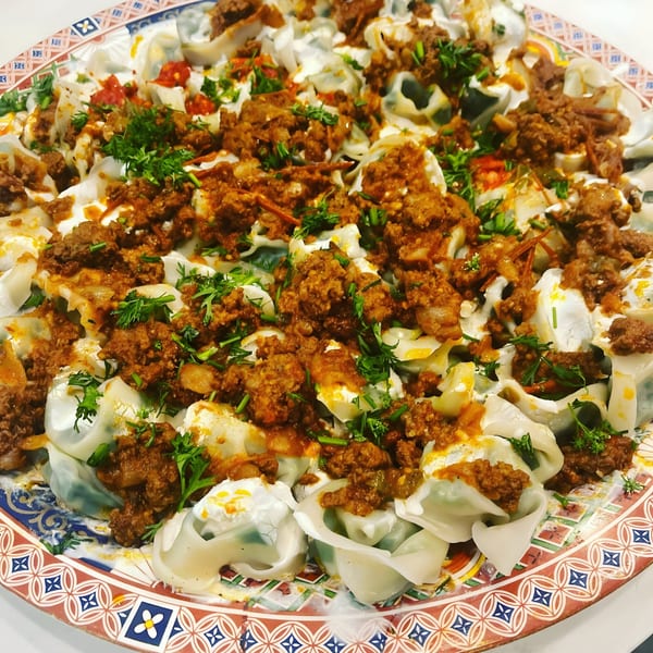 A large platter of Afghan Mantu dumplings, topped with ground meat sauce, yogurt, and fresh herbs.