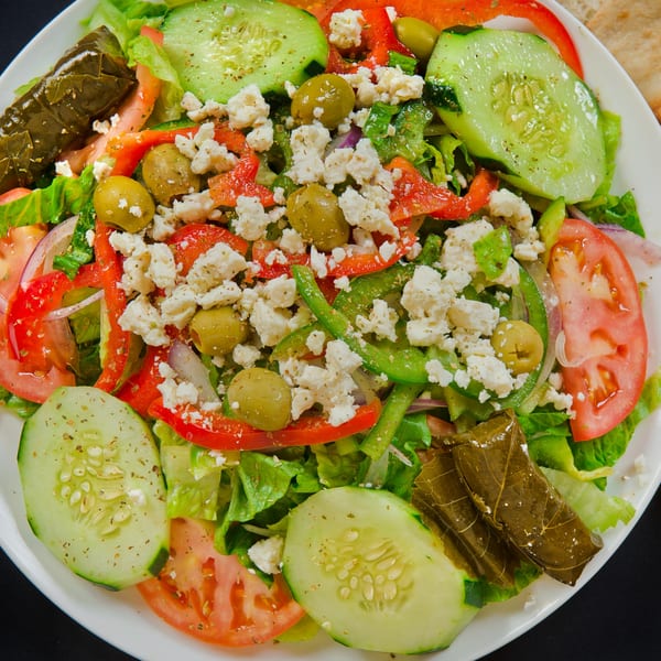 A vibrant salad with lettuce, cucumbers, tomatoes, bell peppers, feta, olives, and stuffed grape leaves.